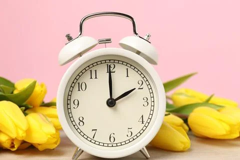 Spring time. Alarm clock and beautiful tulips on table against pink backgro.. Stock Photos