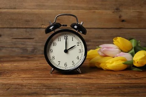 Spring time. Alarm clock and beautiful tulips on wooden table Foto stock