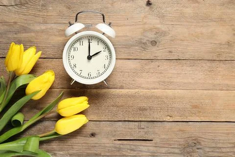 Spring time. Alarm clock and beautiful tulips on wooden table, flat lay. Sp.. Stock Photos