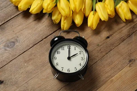 Spring time. Alarm clock and beautiful tulips on wooden table, above view Stock Photos