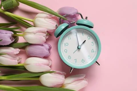 Spring time. Alarm clock and beautiful tulips on pink background, flat lay Foto stock