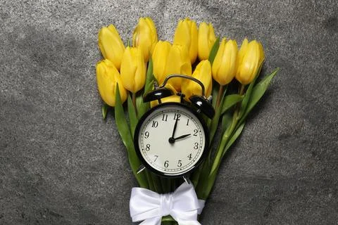 Spring time. Alarm clock and beautiful tulips on grey table, flat lay 스톡 사진