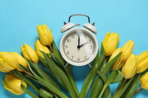 Spring time. Alarm clock and beautiful tulips on light blue background, fla.. 스톡 사진