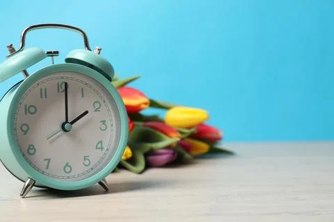 Spring time. Alarm clock and beautiful tulips on wooden table against light.. 스톡 사진