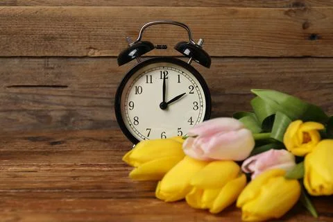 Spring time. Alarm clock and beautiful tulips on wooden table Stock Photos