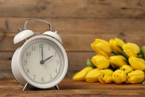 Spring time. Alarm clock and beautiful tulips on wooden table Foto stock