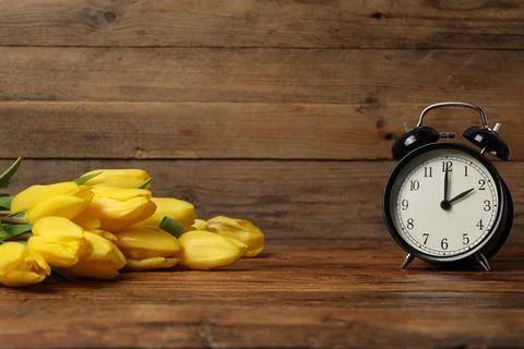 Spring time. Alarm clock and beautiful tulips on wooden table Stock Photos