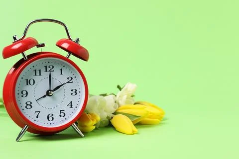 Spring time. Alarm clock and beautiful flowers on green background, space f.. 写真素材