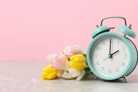 Spring time. Alarm clock and beautiful tulips on grey marble table against .. Foto stock