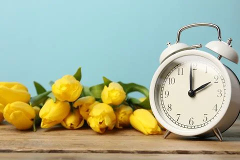 Spring time. Alarm clock and beautiful tulips on wooden table against light.. 写真素材