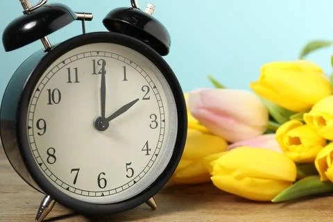 Spring time. Alarm clock and beautiful tulips on wooden table against light.. Foto stock