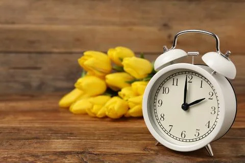 Spring time. Alarm clock and beautiful tulips on wooden table, space for text Foto stock
