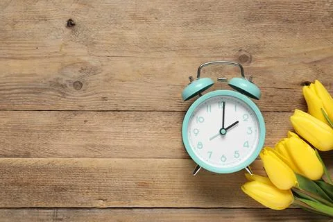 Spring time. Alarm clock and beautiful tulips on wooden table, flat lay. Sp.. Stock Photos