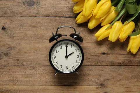 Spring time. Alarm clock and beautiful tulips on wooden table, flat lay Foto stock