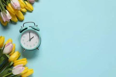Spring time. Alarm clock and beautiful tulips on light blue background, fla.. Stock Photos