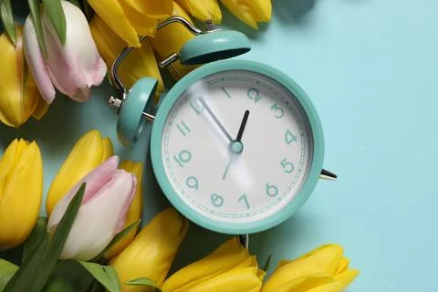 Spring time. Alarm clock and beautiful tulips on light blue background, fla.. 写真素材