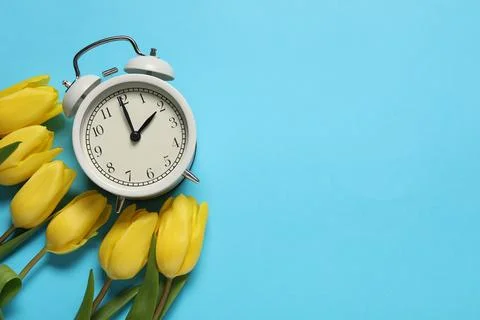 Spring time. Alarm clock and beautiful tulips on light blue background, fla.. Stock Photos
