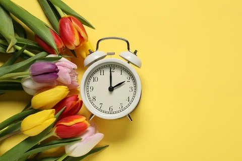 Spring time. Alarm clock and beautiful tulips on yellow background, flat la.. 스톡 사진