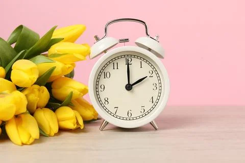 Spring time. Alarm clock and beautiful tulips on wooden table against pink .. Foto stock