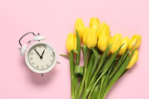 Spring time. Alarm clock and beautiful tulips on pink background, flat lay Stock Photos