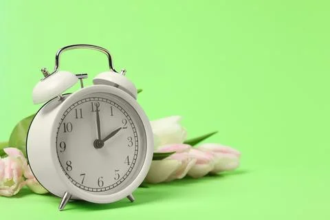 Spring time. Alarm clock and beautiful tulips on green background, space fo.. Stock Photos