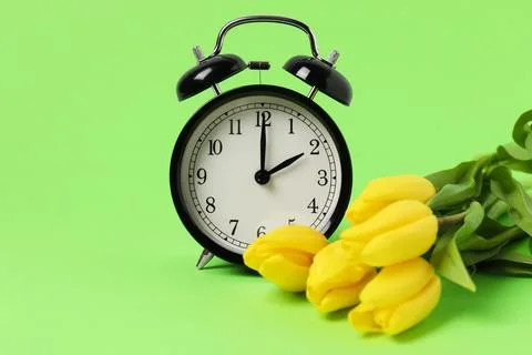 Spring time. Alarm clock and beautiful tulips on green background 스톡 사진