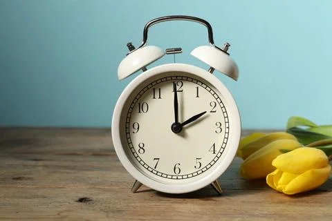 Spring time. Alarm clock and beautiful tulips on wooden table against light.. Foto stock