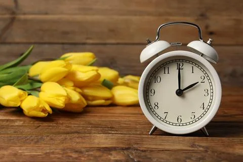 Spring time. Alarm clock and beautiful tulips on wooden table Foto stock