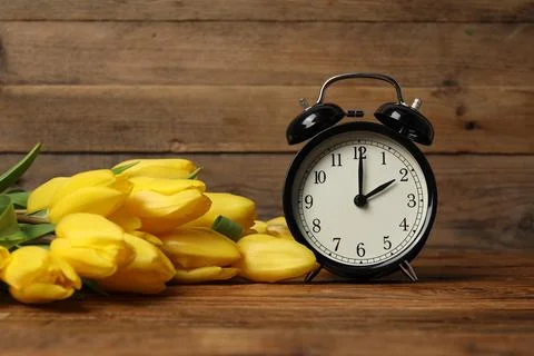 Spring time. Alarm clock and beautiful tulips on wooden table Stock Photos