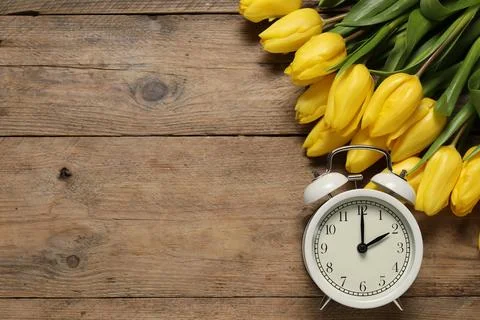 Spring time. Alarm clock and beautiful tulips on wooden table, flat lay. Sp.. Stock Photos