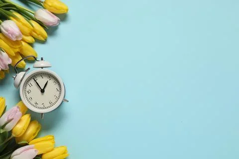 Spring time. Alarm clock and beautiful tulips on light blue background, fla.. Foto stock