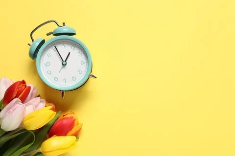 Spring time. Alarm clock and beautiful tulips on yellow background, flat la.. 스톡 사진
