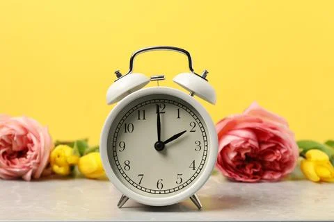 Spring time. Alarm clock and beautiful flowers on grey marble table against.. Stock Photos