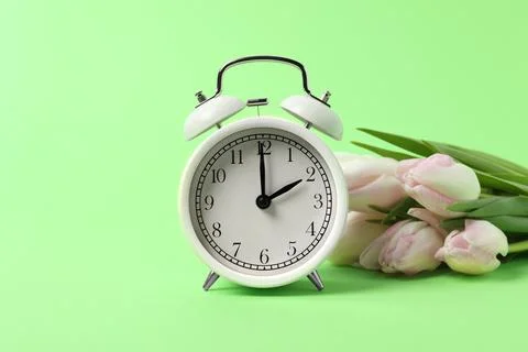Spring time. Alarm clock and beautiful tulips on green background Stock Photos