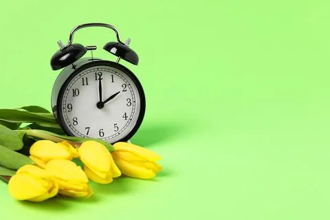 Spring time. Alarm clock and beautiful tulips on green background, space fo.. Stock Photos