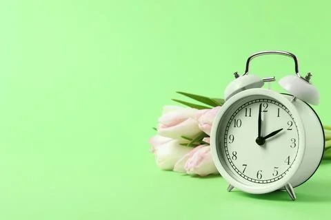 Spring time. Alarm clock and beautiful tulips on green background, space fo.. Stock Photos