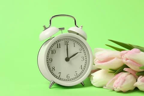 Spring time. Alarm clock and beautiful tulips on green background Stock Photos