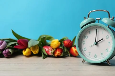 Spring time. Alarm clock and beautiful tulips on wooden table against light.. 写真素材
