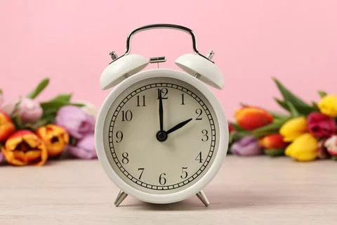 Spring time. Alarm clock and beautiful tulips on wooden table against pink .. Stock Photos