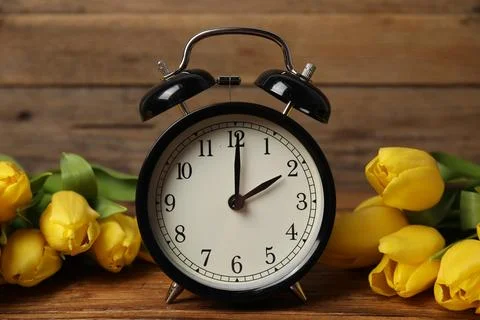 Spring time. Alarm clock and beautiful tulips on wooden table Stock Photos