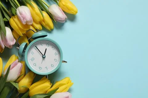 Spring time. Alarm clock and beautiful tulips on light blue background, fla.. 스톡 사진