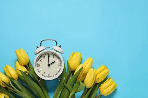 Spring time. Alarm clock and beautiful tulips on light blue background, fla.. 스톡 사진