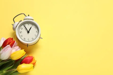 Spring time. Alarm clock and beautiful tulips on yellow background, flat la.. 写真素材