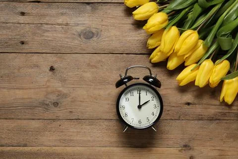 Spring time. Alarm clock and beautiful tulips on wooden table, flat lay. Sp.. Foto stock