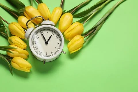 Spring time. Alarm clock and beautiful tulips on green background, flat lay.. Stock Photos
