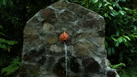 Spring water flows from the stone wall and the jug is made by hand Stock Footage 110754873