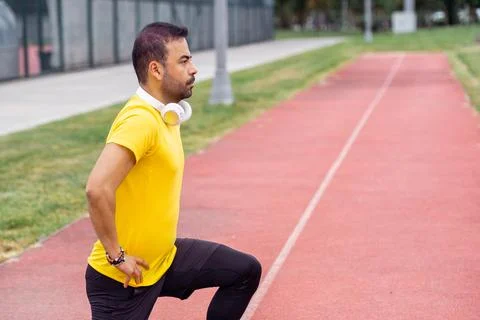 Springtime regular workout, sportive man performs squats on running track at Stock Photos