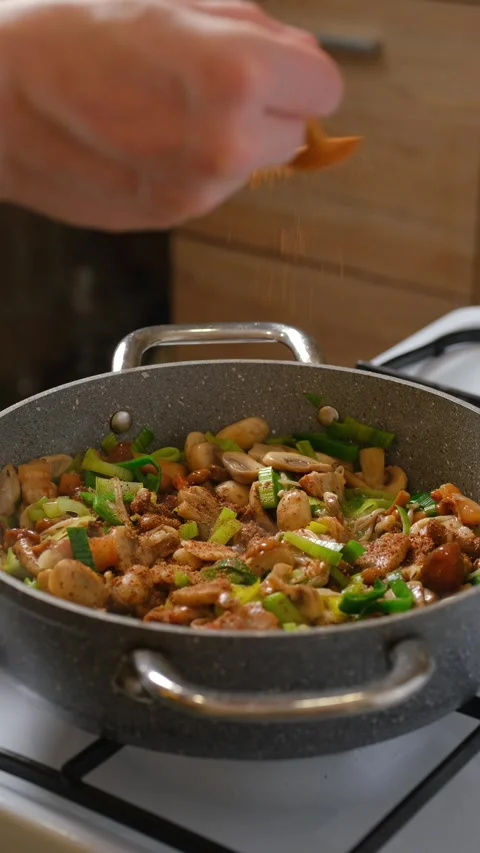 Sprinkle spice over the steaming mushrooms, leeks and bacon in  a frying pan Stock Footage 321680698