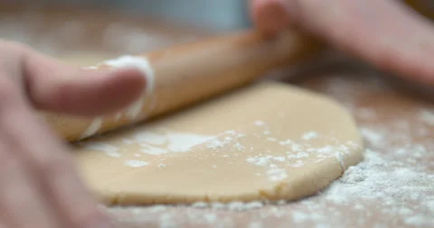 Sprinkled flour drops onto dough being rolled with a rolling pin by a pastry che Stock Footage 199461013