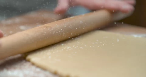 Sprinkled flour drops onto dough being rolled with a rolling pin by a pastry che Stock Footage 199463156
